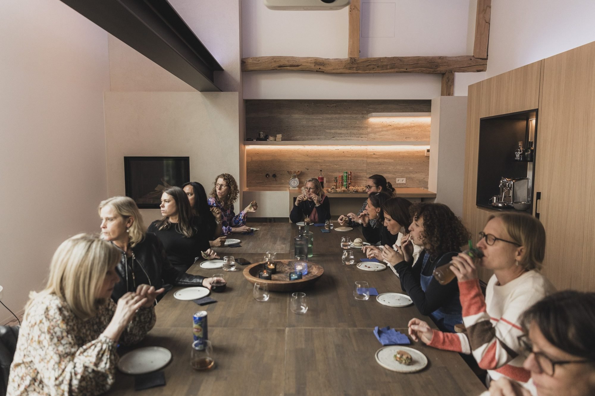 Deelnemers eten samen een broodje aan de lange tafel tijdens de middagpauze